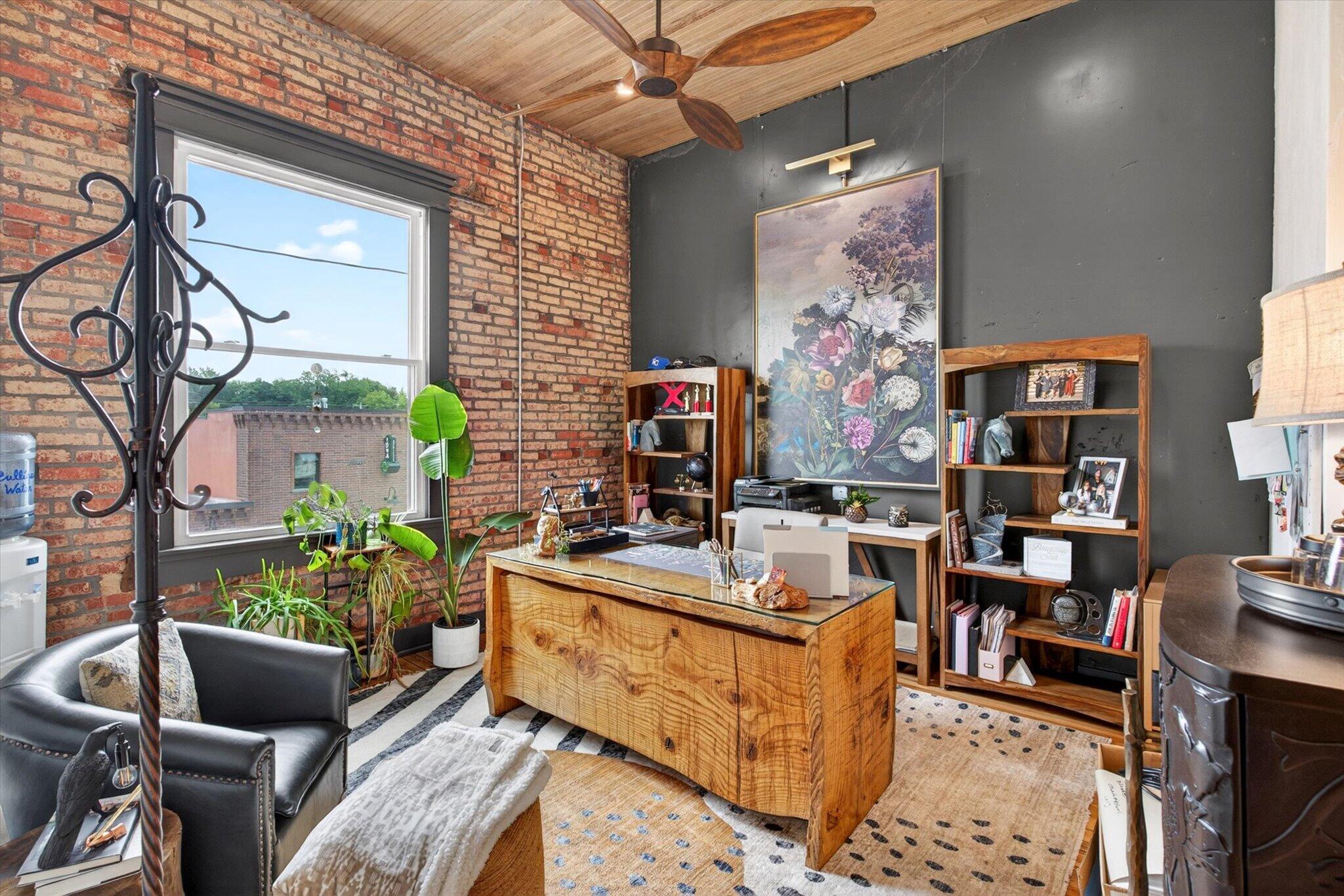 Office 1 in Nixa with exposed brick, a wood ceiling, a large window, and a wooden desk