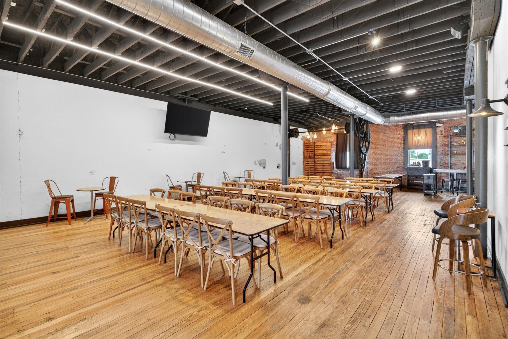 The current open gathering room arranged with wooden tables and chairs
