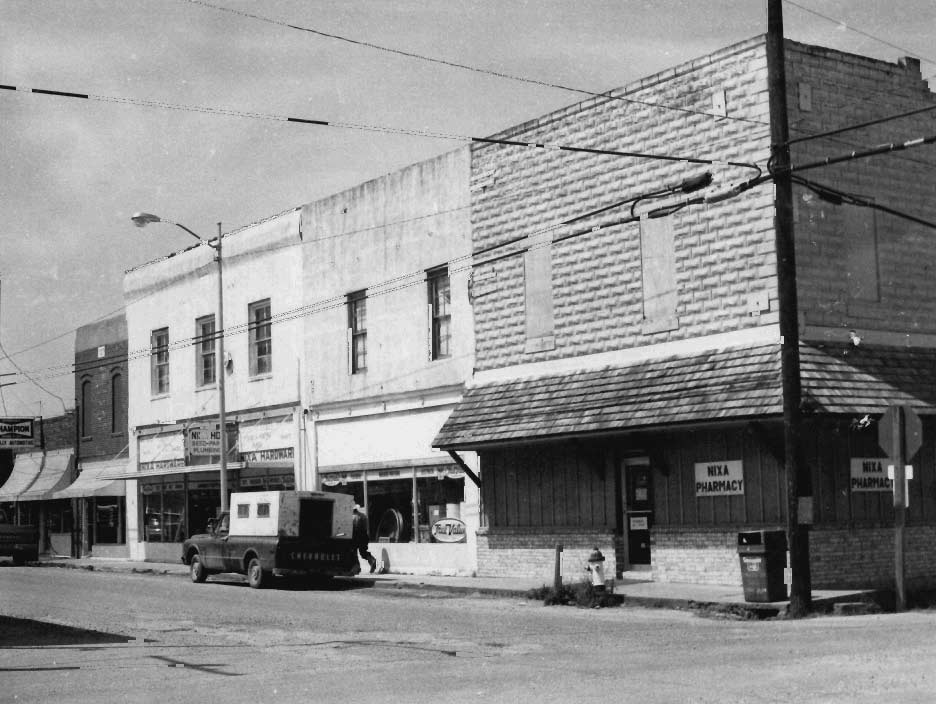 Black-and-white Main Street photograph showing Nixa Hardware at left-center beside Nixa Pharmacy on the corner